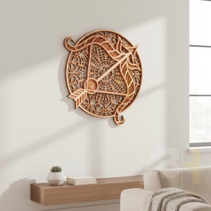 May include: A layered wooden wall art piece depicting the Sagittarius zodiac symbol. The design features a bow and arrow within a circular frame with intricate cut-out patterns. The artwork is made of light and dark brown wood and is mounted on a white wall.