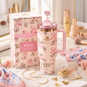 May include: A pink Stanley Quencher H2.0 Tumbler with a floral and bow design, a matching gift box, and a pink handle. The tumbler has a capacity of 40 oz. and features the text "LOVESHACKFANCY".