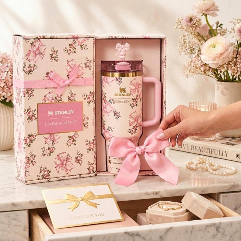 May include: A pink floral-patterned Stanley tumbler with a matching gift box. The tumbler has a handle and a straw. The gift box is tied with a pink ribbon. The text "Stanley LovesShackFancy" is visible on the box.