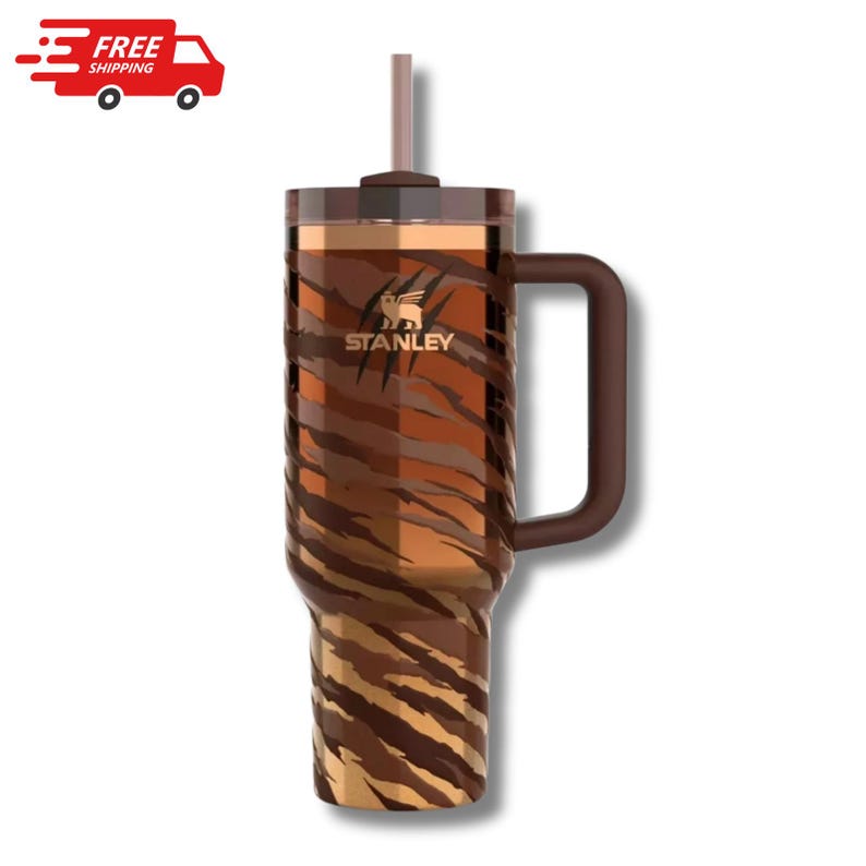K&ouml;nnte beinhalten: Ein brauner und goldener Stanley-Becher mit Tigerstreifenmuster. Der Becher hat einen Griff, einen Strohhalm und das Stanley-Logo. Der Becher ist f&uuml;r kalte Getr&auml;nke konzipiert.