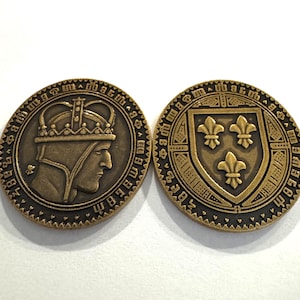 May include: Two antique bronze-colored coins. One coin features a profile of a crowned figure. The other coin displays a shield with three fleur-de-lis symbols. Both coins have an outer ring with an inscription.
