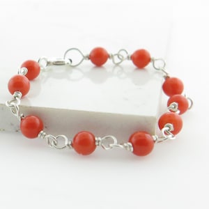 Puede incluir: Un brazalete de cadena de plata con cuentas naranjas. El brazalete tiene un cierre de broche.