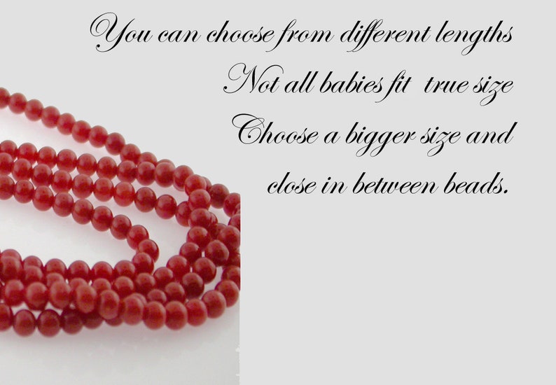 Puede incluir: Primer plano de una hebra de cuentas de coral rojo. Las cuentas son redondas y lisas, y est&aacute;n enhebradas en un hilo transparente. El texto "You can choose from different lengths. Not all babies fit true size. Choose a bigger size and close in between beads." est&aacute; escrito en letra cursiva.