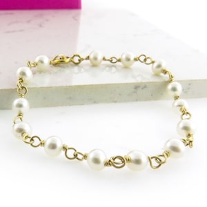May include: A delicate gold chain bracelet with white pearls. The pearls are evenly spaced and the chain is made of thin wire.