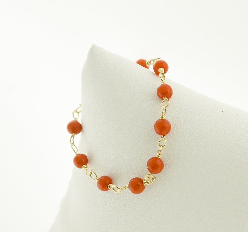 Puede incluir: Un brazalete de cadena de oro con cuentas de coral naranja.