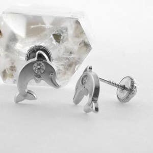 Puede incluir: Un par de pendientes de plata con forma de delfín con un strass transparente en cada delfín. Los pendientes tienen un cierre de rosca.