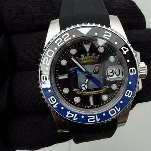 May include: A stainless steel wristwatch with a black rubber strap and a black dial featuring a crest and the text FULMINEO FUOCO DI FULMINEA SOL. The bezel is black and blue with white numerals, and the date window displays the number 30.