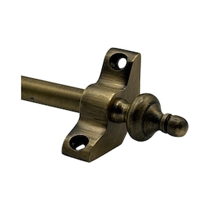 May include: Antique brass curtain rod hardware with a decorative finial. The hardware features a square mounting bracket with two holes and a rod extending to the left. The finial is a rounded shape with a small ball at the end.