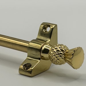 May include: A brass curtain rod with a pineapple finial. The rod features a rectangular mounting bracket with screw holes. The pineapple finial adds a decorative element. The curtain rod is designed for window treatments.