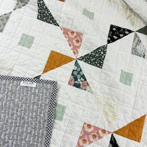 Puede incluir: Una colcha blanca con un diseño de patchwork que presenta varios patrones florales en tonos de verde, rosa, naranja y blanco. La colcha está hecha con una variedad de telas y tiene una estética simple y moderna.