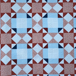 Op de afbeelding: Een quilt met een geometrisch patroon van rode, blauwe en witte vierkanten en driehoeken. De quilt is gemaakt van katoenen stof en heeft een gestikt ontwerp.
