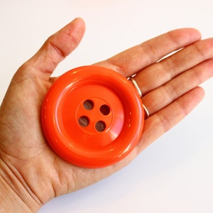 Peut inclure: Un grand bouton en plastique orange vif à quatre trous.