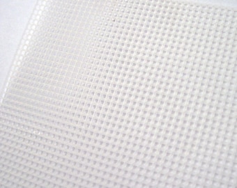 Puede incluir: Primer plano de una lámina de plástico blanco. La lámina tiene un patrón de rejilla de agujeros cuadrados espaciados uniformemente. El material parece translúcido y la lámina está ligeramente inclinada, mostrando su textura y profundidad.