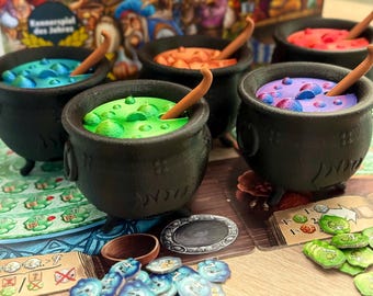 May include: A tabletop game featuring five black cauldrons filled with colorful concoctions. Each cauldron holds a different colored liquid, including blue, green, orange, purple, and red, with a wooden spoon. Game pieces and cards are scattered around.