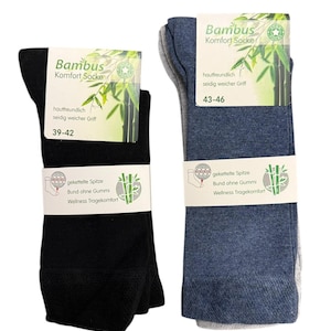 Könnte beinhalten: Zwei Paar Socken, eines in Schwarz und eines in Blau, werden gezeigt. Jedes Paar ist mit einem Etikett verpackt, das den Text "Bambus Komfort Socke" und Bambusbilder zeigt. Die Etiketten weisen auch die Größen 39-42 und 43-46 aus.