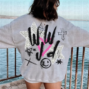 Puede incluir: Sudadera gris claro con un dise&ntilde;o gr&aacute;fico en la espalda. El dise&ntilde;o incluye las palabras "WILD" en negro y rosa, junto con varios s&iacute;mbolos como una cruz, un rayo y una carita sonriente. La sudadera tiene cuello redondo.