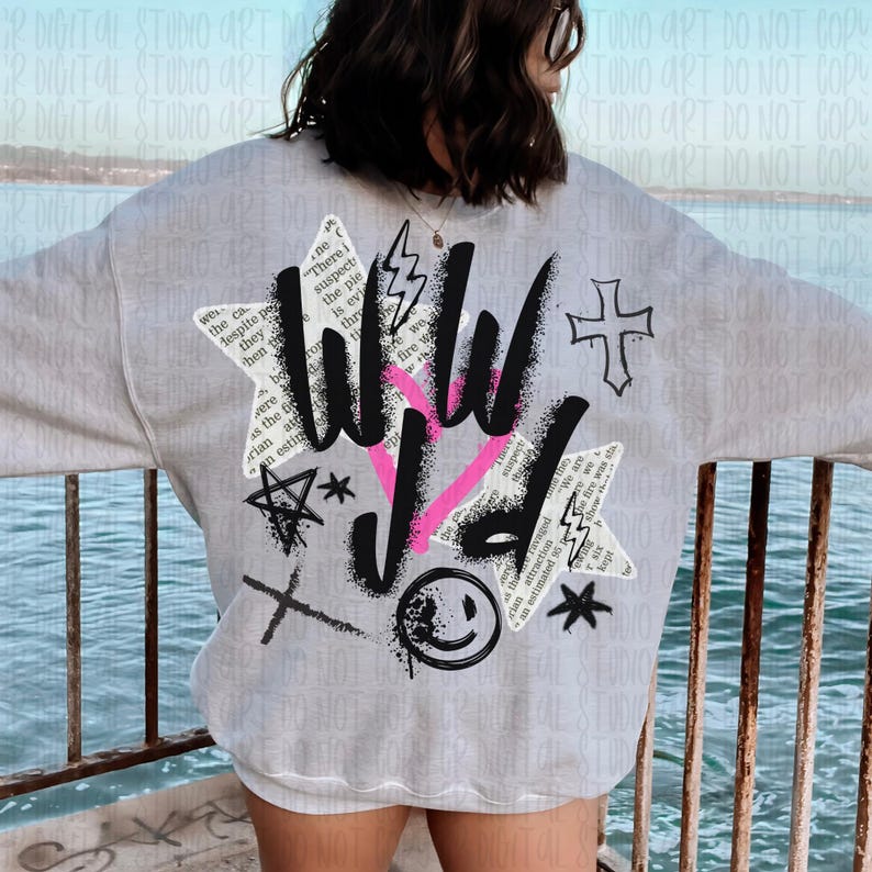 Puede incluir: Sudadera gris claro con un dise&ntilde;o gr&aacute;fico en la espalda. El dise&ntilde;o incluye las palabras "WILD" en negro y rosa, junto con varios s&iacute;mbolos como una cruz, un rayo y una carita sonriente. La sudadera tiene cuello redondo.