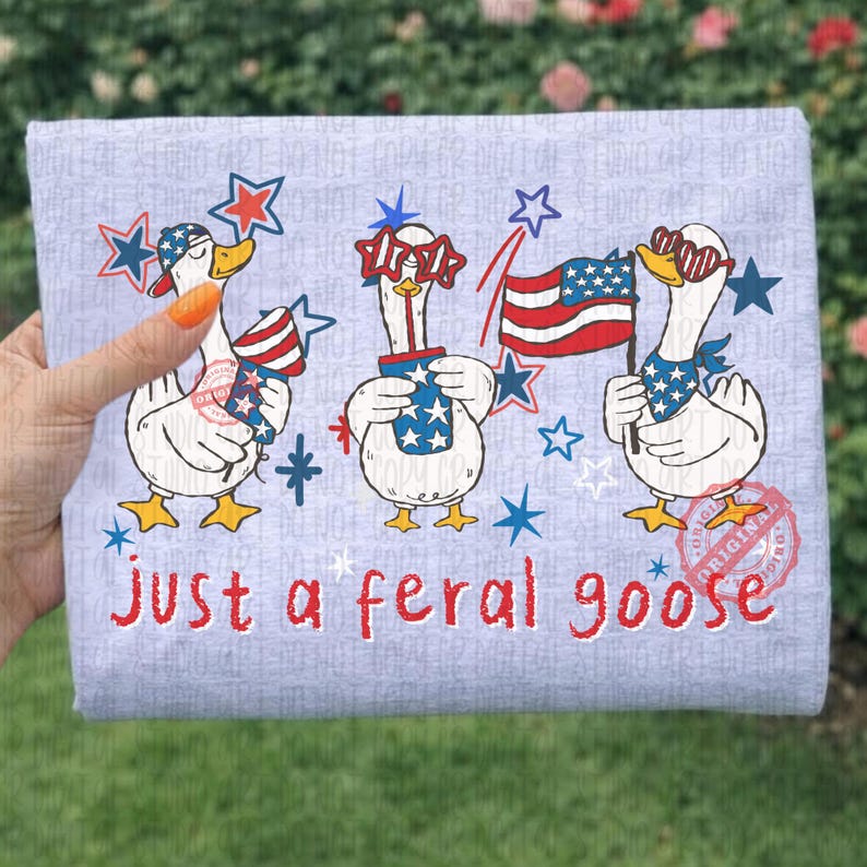 K&ouml;nnte beinhalten: Ein hellgrauer Stoff mit einer skurrilen Illustration von drei Comic-G&auml;nsen mit patriotischem Zubeh&ouml;r. Die G&auml;nse halten Feuerwerk und Flaggen, mit dem Text "just a feral goose" in Rot.