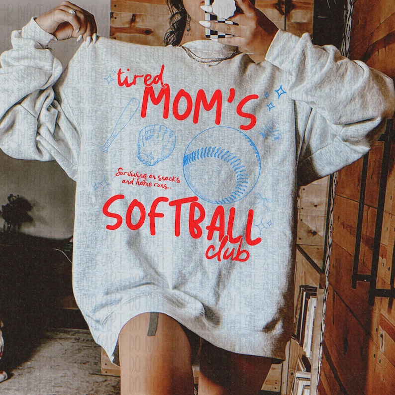 K&ouml;nnte beinhalten: Ein hellgraues Sweatshirt mit den roten Worten "tired MOM'S SOFTBALL club" und blauen Baseball-Grafiken. Der Text "Surviving on snacks and home runs" ist ebenfalls enthalten. Das Sweatshirt hat einen l&auml;ssigen, sportlichen Stil.