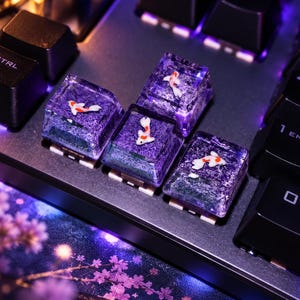 Puede incluir: Cuatro teclas mecánicas translúcidas de color morado con peces koi en miniatura de color blanco y naranja incrustados en la resina. Las teclas están instaladas en un teclado negro con retroiluminación morada junto a teclas negras estándar.