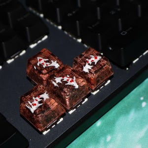 May include: Four custom keycaps with a brown and translucent design, featuring white and red accents, rest on a black keyboard. The keycaps are square and appear to be made of resin or a similar material. The keyboard is black with white key markings.