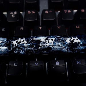 May include: A custom keycap with a blue and white marbled effect, set on a black keyboard. The keycap's design is artistic and unique, enhancing the keyboard's aesthetic appeal. The keyboard keys are black.