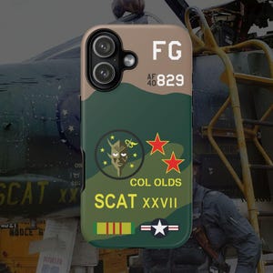 May include: A phone case with a camouflage pattern in shades of green and tan. The case features the text "FG", "AF 40 829", "COL OLDS", and "SCAT XXVII". It also has a devil graphic and red star designs.