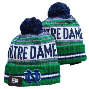 Op de afbeelding: Twee gebreide mutsen met een donkerblauwe pompon aan de bovenkant. De mutsen zijn gestreept in donkerblauw, wit en groen. De tekst NOTRE DAME is in donkerblauw gebreid op een witte band. Een blauw ND-logo is geborduurd op de groene geribbelde boord.