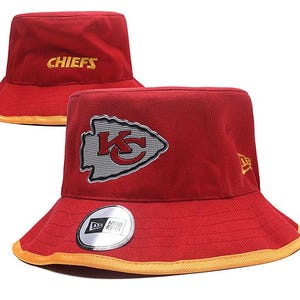 Op de afbeelding: Rode vissershoed met het woord "CHIEFS" in goud geborduurd. De hoed heeft het teamlogo op de voorkant en een New Era-sticker. De rand heeft een gouden rand.