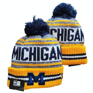 May include: Two knit beanies featuring a navy blue pom-pom on top. The hats have horizontal stripes in navy blue, white, and yellow. The word MICHIGAN is knitted in navy blue letters across the center, and a navy blue M logo is on the yellow cuff.