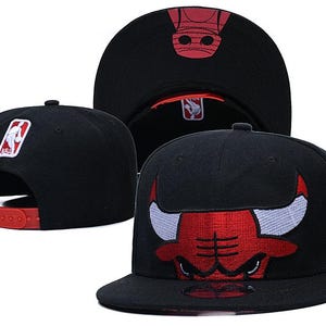 Pode incluir: Um boné snapback preto com um logótipo dos Chicago Bulls bordado a vermelho e branco na parte da frente, uma correia de plástico ajustável vermelha na parte de trás e um pequeno emblema com o logótipo da NBA por cima da abertura.