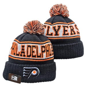 May include: Two black knit beanies with orange and white pom-poms. The front features the Philadelphia Flyers logo and the text Philadelphia Flyers in orange and white lettering. A New Era tag is attached to the cuff of the front beanie.