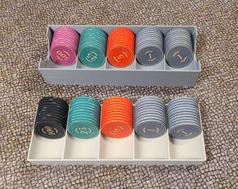 May include: Poker chips in a gray plastic organiser. The chips are various colours, including pink, teal, orange, and grey, with denominations of 1, 5, 25, 100, and 500. The chips are arranged in two trays.