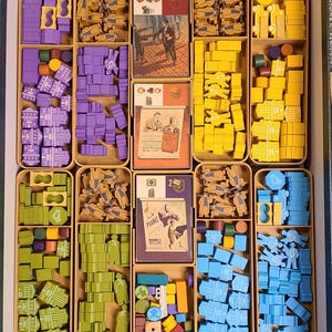 May include: A board game organizer filled with various game pieces in shades of purple, yellow, green, and blue. The organizer includes cards with illustrations and text, and wooden tokens. The game pieces are arranged in individual compartments.