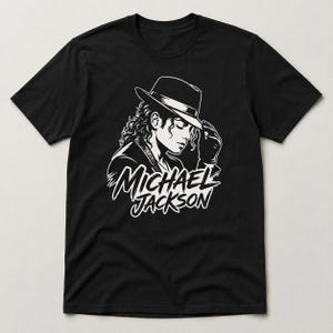 May include: Black t-shirt featuring a white graphic of Michael Jackson in a hat, with the text "MICHAEL JACKSON" below the image. The design is a stylized illustration of the singer.
