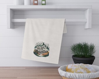 May include: White kitchen towel with the text "Go Tell it on the Mountain" in a mountain and forest design. The towel is hanging on a white shelf with jars and spices.