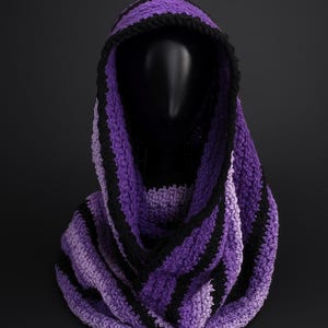 Peut inclure: Un capuchon crocheté à la main dans les tons de violet et de noir. Le capuchon présente des rayures alternées de fil violet et noir, avec une bordure noire autour de l'ouverture du capuchon. L'article est présenté sur une tête de mannequin noire.