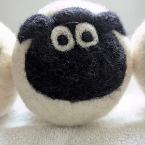 Peut inclure: Gros plan sur une tête de mouton en feutre blanc et noir. Le mouton a un visage et des oreilles noirs, des yeux blancs et un corps blanc. Fabriqué en laine, il présente un aspect doux et texturé. L'image est bien éclairée, révélant les détails.