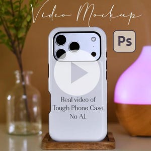 Könnte beinhalten: Eine weiße Handyhülle mit einem Video-Play-Button, dem Text "Real video of Tough Phone Case No AI" und einem Photoshop-Logo. Eine kleine Vase mit Grün und ein rosa-brauner ätherischer Öl-Diffusor sind ebenfalls im Bild.