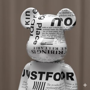 May include: A white bear-shaped figurine with black text and newspaper-style print. The text includes the words "KIN," "PLACE," "RIBING IS RELLARE," and "JUSTFOOR." The figurine has a glossy finish and a modern aesthetic.