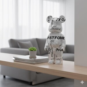 May include: A white and black bear-shaped figurine with text printed on its surface stands on a light wood table. The text includes the words "JUSTFOOR" and "RIBING IS." A small potted plant and a stack of magazines are also on the table.