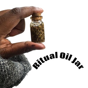Puede incluir: Un pequeño frasco de vidrio lleno de hierbas secas y aceite, sellado con un tapón de corcho. Las palabras "Ritual Oil Jar" están arqueadas en la parte inferior de la imagen en texto negro. El frasco se sostiene sobre un fondo blanco.