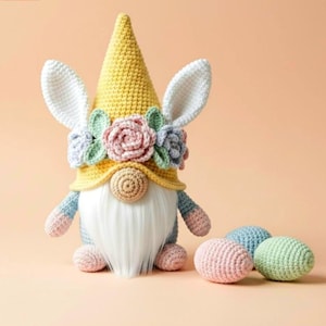 May include: A handmade Easter gnome with bunny ears, a yellow hat, and a white beard. The gnome is decorated with a floral crown and has blue and pink arms and feet. Three crocheted eggs in pastel colors are next to the gnome.