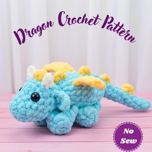 May include: A handmade blue crochet dragon with yellow wings and accents. The dragon has black eyes and white horns. The text "Dragon Crochet Pattern" is above the dragon. A purple badge with the text "No Sew" is in the bottom right corner.