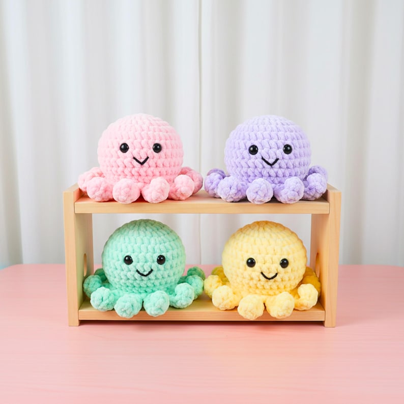 May include: Four crocheted octopus plush toys in pastel colors: pink, purple, mint green, and yellow. Each octopus has a smiling face and eight tentacles. They are displayed on a small, light-colored wooden shelf.