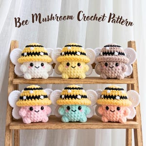 May include: Six colorful crochet mushroom figures with bee-themed hats and smiling faces are displayed on a wooden shelf. The hats are yellow with black stripes. The text "Bee Mushroom Crochet Pattern" is at the top.
