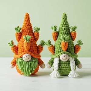 May include: Two crochet gnomes with carrot accents. One gnome is orange with a green beard, the other is green with white braids. Both have carrot decorations on their hats. The gnomes are on a white surface with a light green background.