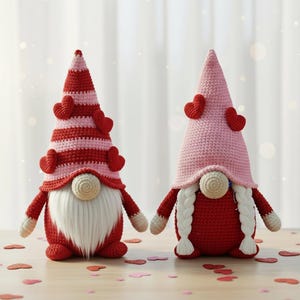 May include: Two handmade crochet gnomes. One gnome has a red and pink striped hat with red hearts, a white beard, and a red body. The other gnome has a pink hat with red hearts, white braids, and a red body. Decorative items.