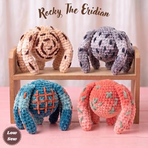 May include: Four plush toys titled Rocky The Eridian, each with a round body and multiple legs. One is beige with brown swirls, one is grey with dark spots, one is blue with an orange grid pattern, and one is coral with green cross stitches.