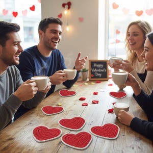 K&ouml;nnte beinhalten: Eine Gruppe von Menschen sitzt an einem Holztisch und genie&szlig;t Kaffee. Rote herzf&ouml;rmige Untersetzer mit wei&szlig;em Rand liegen auf dem Tisch. Eine kleine Tafel zeigt "Happy Valentine's Day".